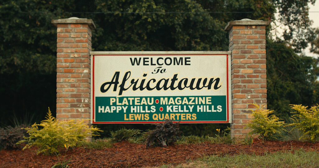 A sign that reads "Welcome to Africatown" and lists the names of the neighborhoods in the community: Plateau, Magazine, Happy Hills, Kelly Hills, Lewis Quarters. 